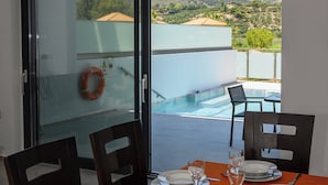 Zona pranzo con tavolo apparecchiato per quattro, con vista su una piscina e un paesaggio montuoso.