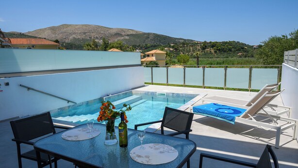 Area piscina sul tetto con tavolo e sedie, ringhiera in vetro e vista sul paesaggio circostante.