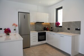 Eine moderne Küche mit weißen Schränken, einem Edelstahl-Kühlschrank, einem Backofen und einem Fenster mit Blick.