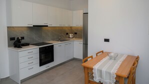 A modern kitchen with white cabinets, a built-in oven, and a dining table with a lace tablecloth. - Herodotos Residence–Peaceful Stay Near Keri Beach (Keri)