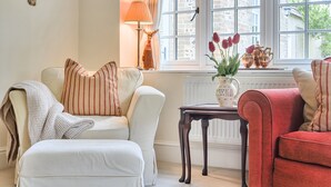 A room with a white sofa, a red sofa, a small table, and a window with a view of buildings. - Piddlehinton Coach House - Piddlehinton, Dorchester, sleeps 6 guests (Piddlehinton)