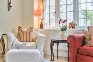 A room with a white sofa, a red sofa, a small table, and a window with a view of buildings. - Piddlehinton Coach House - Piddlehinton, Dorchester, sleeps 6 guests (Piddlehinton)