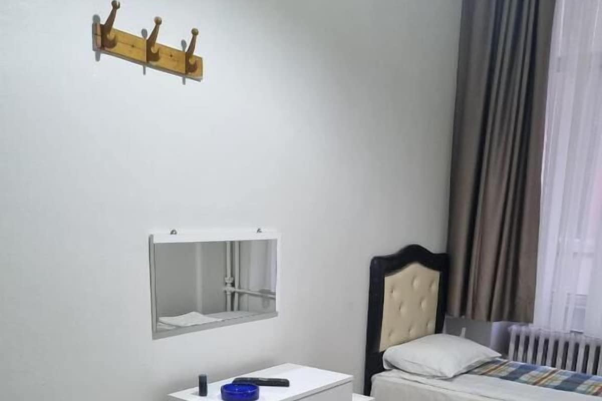 A bedroom with two beds, a small white desk, a mirror, and a window with curtains.
