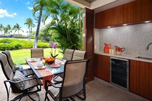 A modern kitchen with a built-in dishwasher, a dining area with a table and chairs, and a view of a tropical garden.