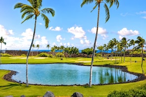A golf course with a water hazard, palm trees, and a clear sky. - Islands at Mauna Lani | Fairway View 2 BR | Car Incl. w/ 6+ Nights | IML-F3 by KBM (Waimea)