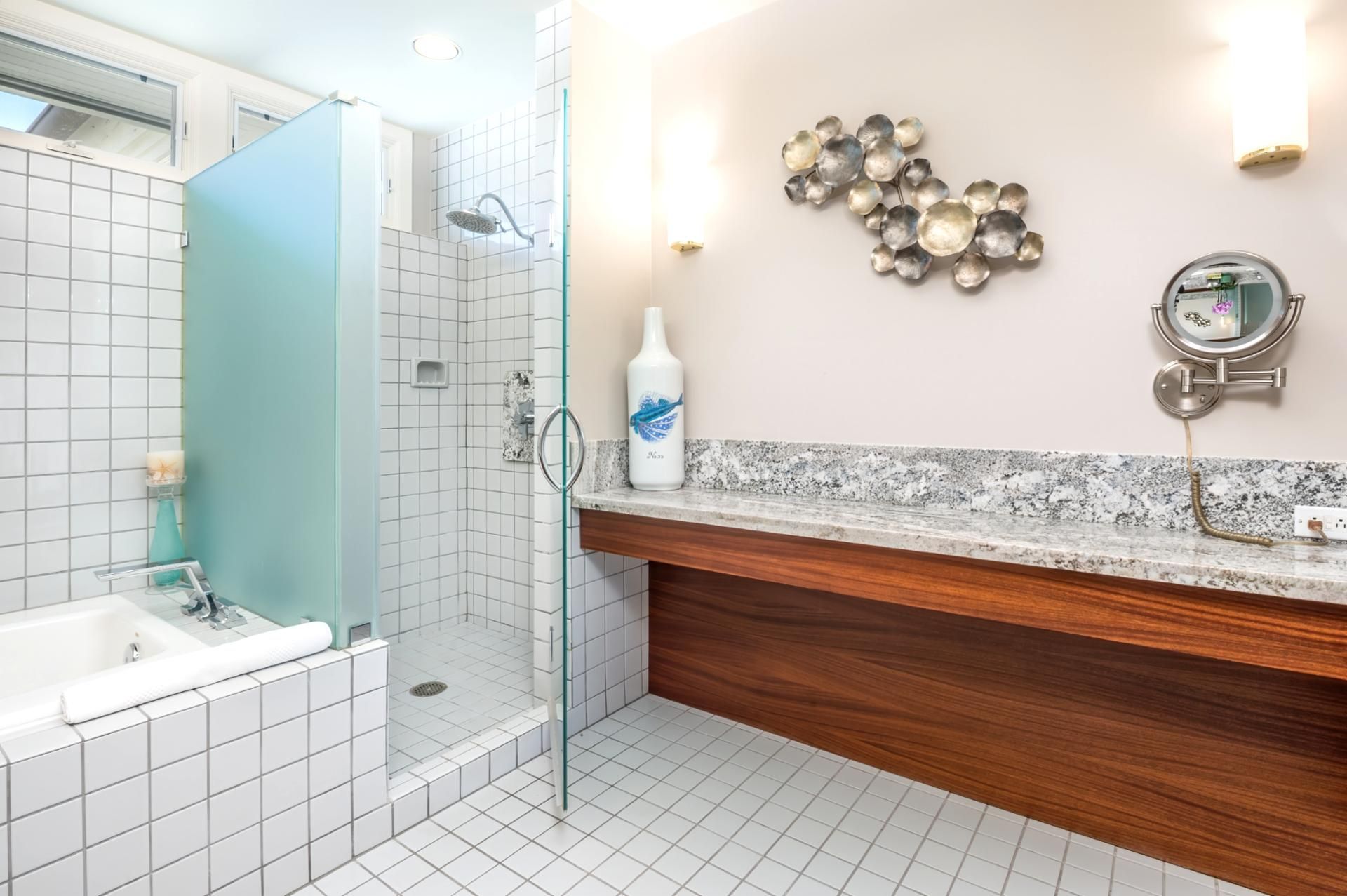 A modern bathroom with a shower, a bathtub, a vanity with a mirror, and a decorative wall piece.