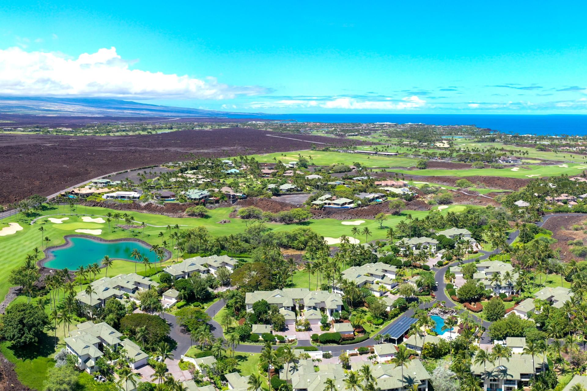 A golf course with a large pond, surrounded by residential buildings with green roofs, and a clear view of the ocean.