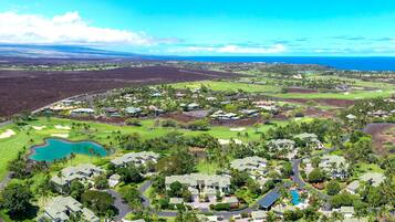 A golf course with a large pond, surrounded by residential buildings with green roofs, and a clear view of the ocean.
