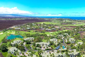 A golf course with a large pond, surrounded by residential buildings with green roofs, and a clear view of the ocean.