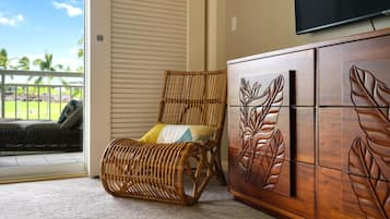 A wicker chair with cushions, a wooden cabinet with leaf designs, and a television mounted on the wall.