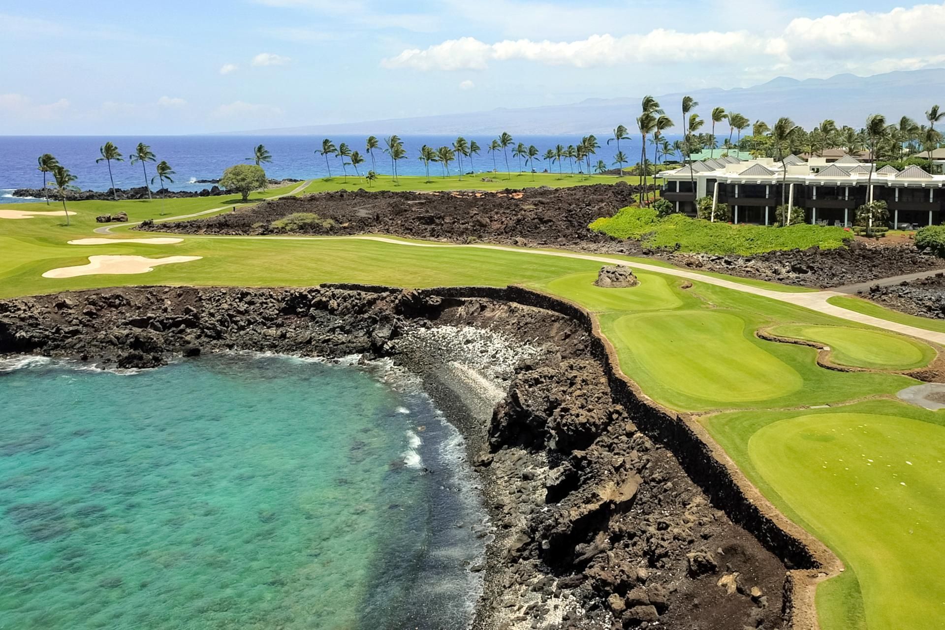A golf course with a view of the ocean and a hotel in the background.