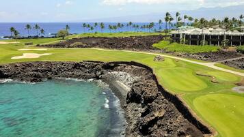 A golf course with a view of the ocean and a hotel in the background.