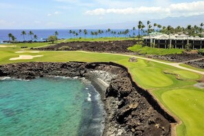 A golf course with a view of the ocean and a hotel in the background.