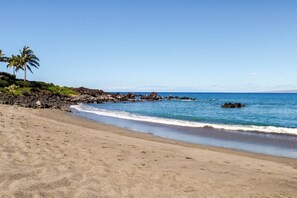 Ein Strand mit klarem, blauem Wasser, einem sandigen Ufer und Felsformationen.