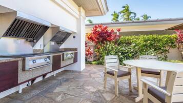 An outdoor kitchen with a grill, stone flooring, and a table with chairs.