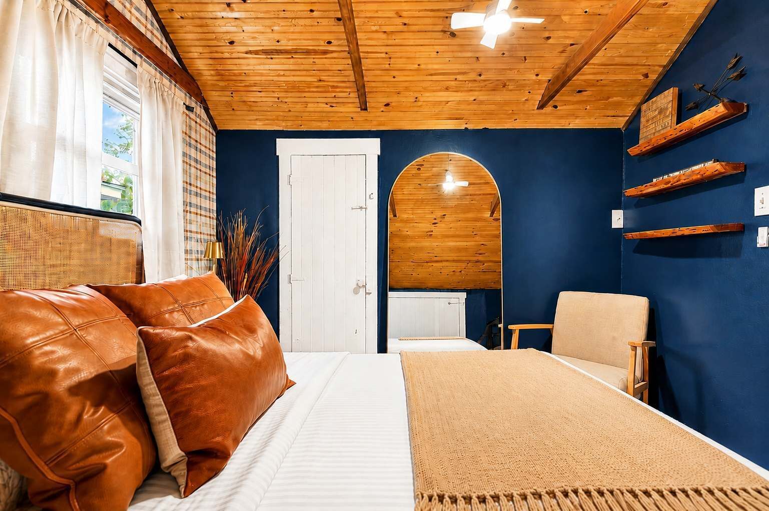 A room with a bed, a chair, a wooden ceiling, and a blue wall.
