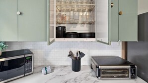 Una cucina con forno a microonde integrato, tostapane e ripiano con bicchieri e pentole.