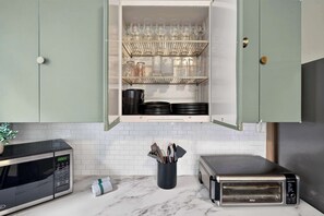 Eine Küche mit Einbau-Mikrowelle, Toaster und einem Regal mit Gläsern und Kochgeschirr.