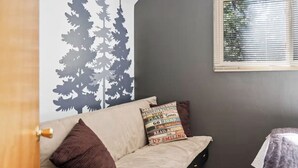 Ett rum med en grå vägg, ett fönster med persienner, en soffa med en kudde och en dörr.