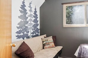 Ein Zimmer mit grauer Wand, einem Fenster mit Jalousien, einem Sofa mit Kissen und einer Tür.
