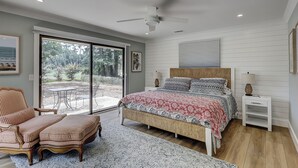 A bedroom with a bed, a chair, a nightstand, and a view of the outdoors. - New Listing! Luxury Updated 4 BR 3 BA Golf View Near the Beach Pool Sea Pines (Hilton Head Island)