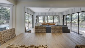 A spacious room with a large wooden table, wicker furniture, and a view of the outdoors through large windows. - New Listing! Luxury Updated 4 BR 3 BA Golf View Near the Beach Pool Sea Pines (Hilton Head Island)