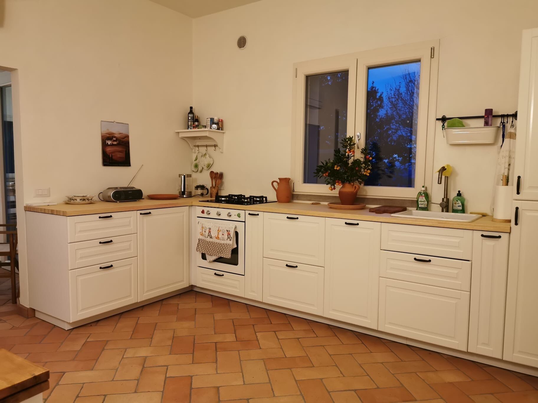 A kitchen with white cabinets, a tiled floor, a stove, and a window with a view of trees.