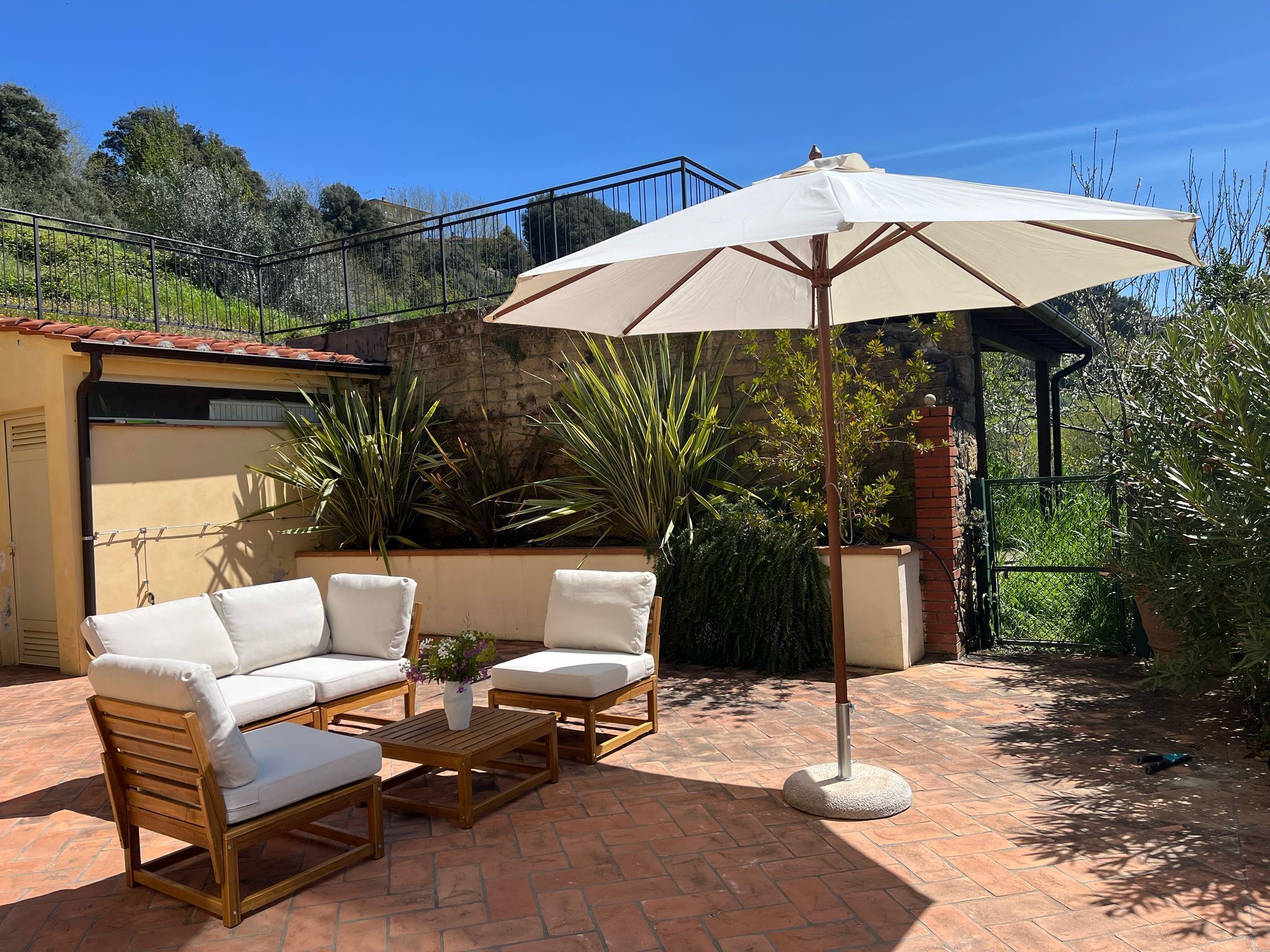 A patio with a beige sofa, two armchairs, a wooden coffee table, and a large umbrella.