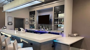 Uma área de bar com um balcão comprido, banquetas e prateleiras com garrafas.