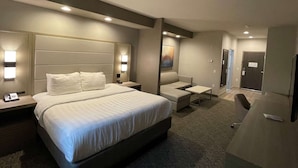 Quarto de hotel com uma cama grande, mesas de cabeceira, uma escrivaninha, uma cadeira e um espelho.