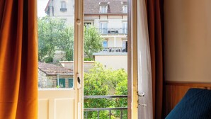 Una camera da letto con un letto, tende e vista sugli edifici attraverso una porta aperta.