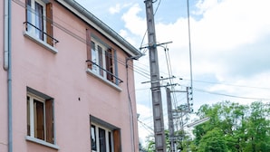 Un edificio rosa con una porta e delle finestre in legno, un palo della luce con fili e una strada.