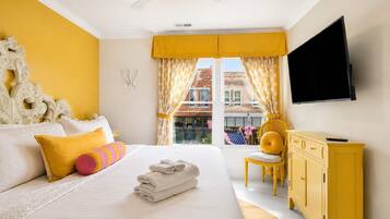 A hotel room with a bed, a television, a window with curtains, a yellow chair, and a yellow cabinet.