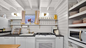 Una cocina con muebles blancos, estufa, lavamanos y una ventana con cortinas.
