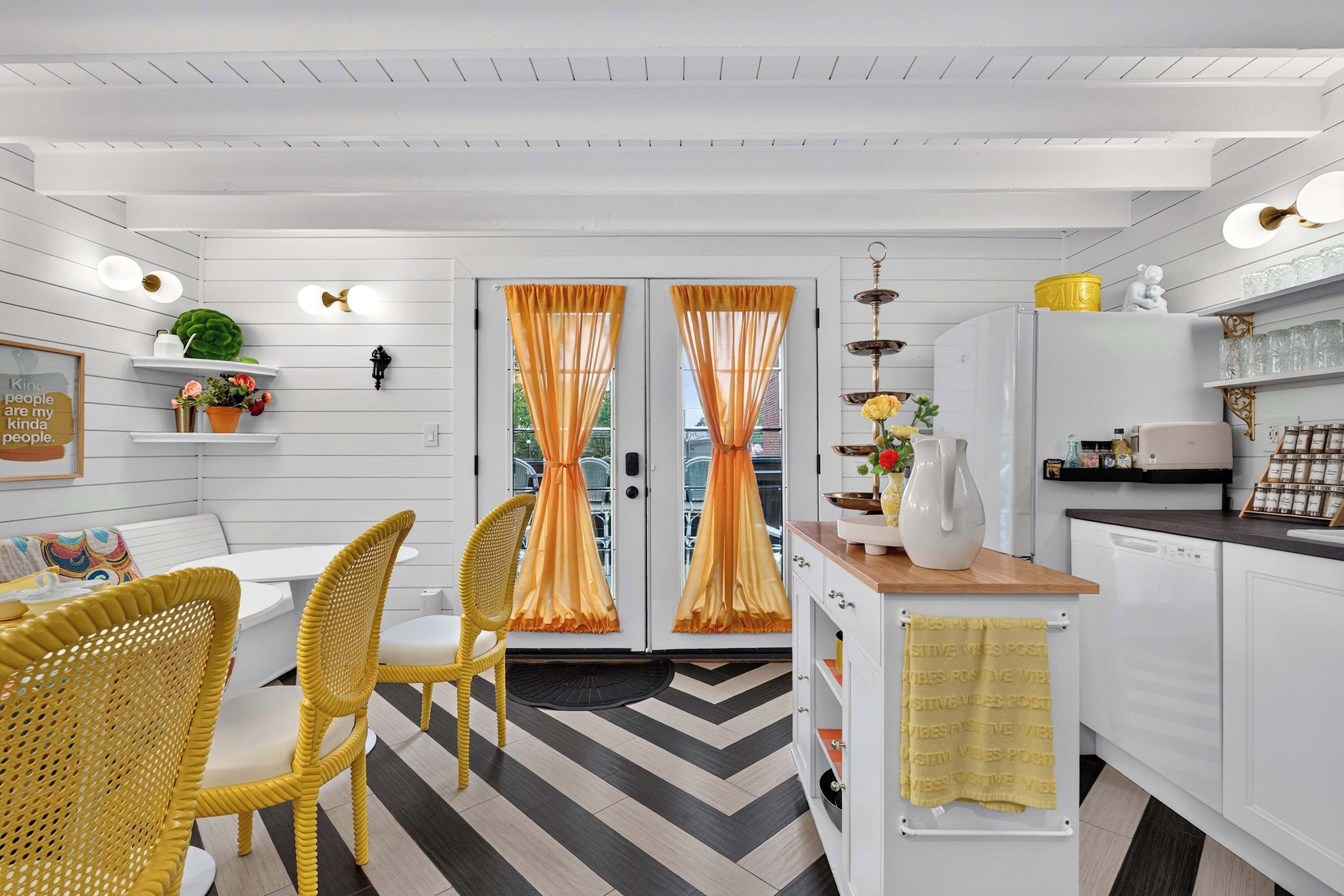 A modern kitchen with white cabinetry, a dining area with wicker chairs, and a herringbone-patterned floor.