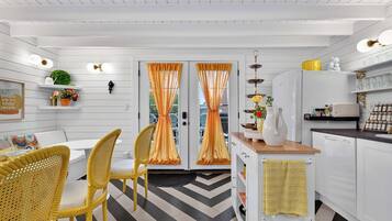 A modern kitchen with white cabinetry, a dining area with wicker chairs, and a herringbone-patterned floor.
