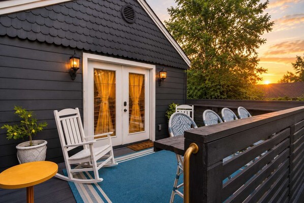 A house with a dark exterior, a white door, and a blue porch with a rocking chair, a small table, and two chairs.