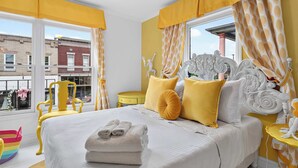 Un dormitorio con una cama grande, cortinas amarillas y vistas a edificios.