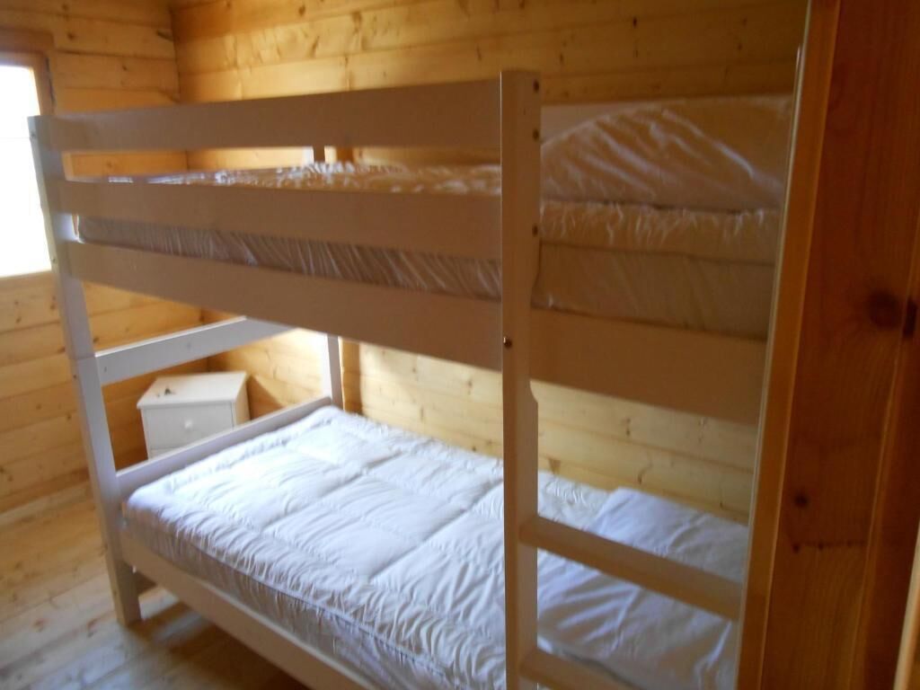 Una habitación tipo cabaña de madera con literas, un pequeño tocador blanco y una ventana.