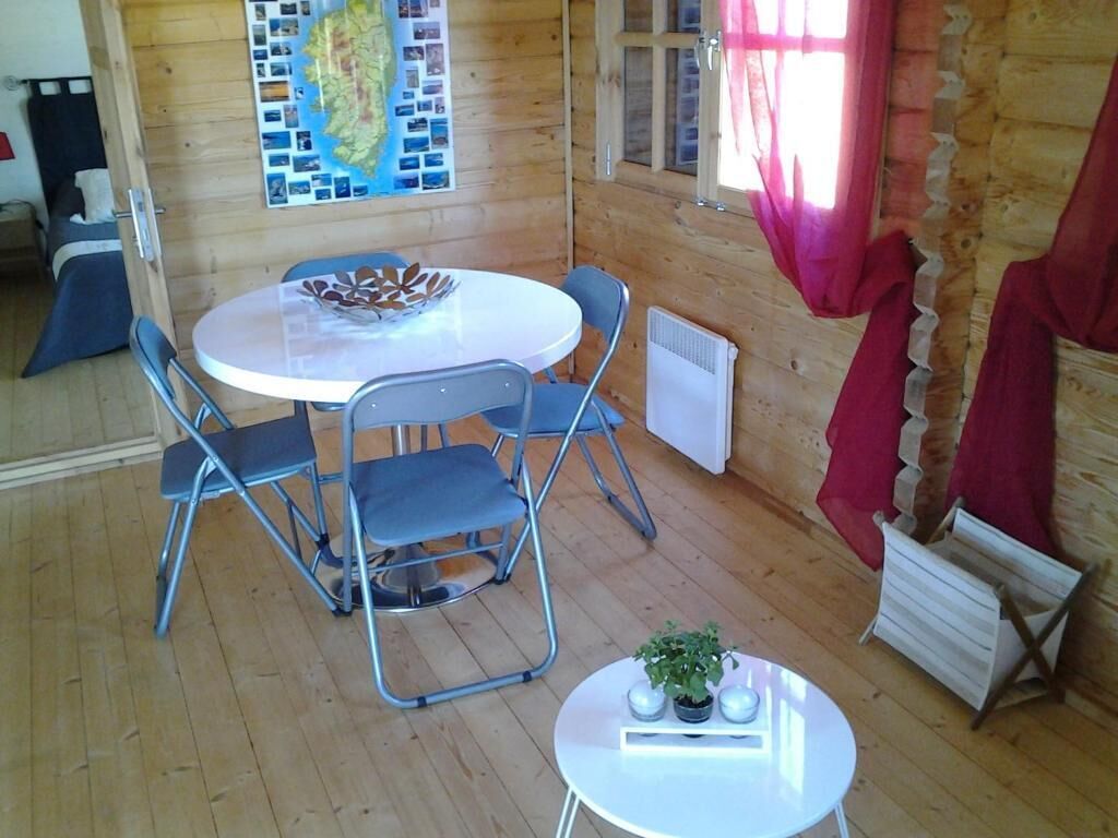 L’intérieur d’un chalet en bois comprend une table de salle à manger ronde, deux chaises, une petite table d’appoint avec une plante et une carte géographique accrochée au mur.
