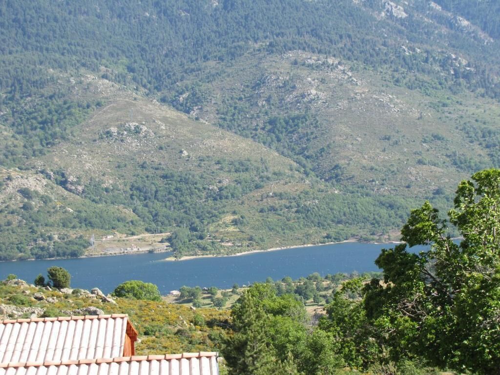 A mountainous landscape with a lake, a red-roofed building, and dense greenery.