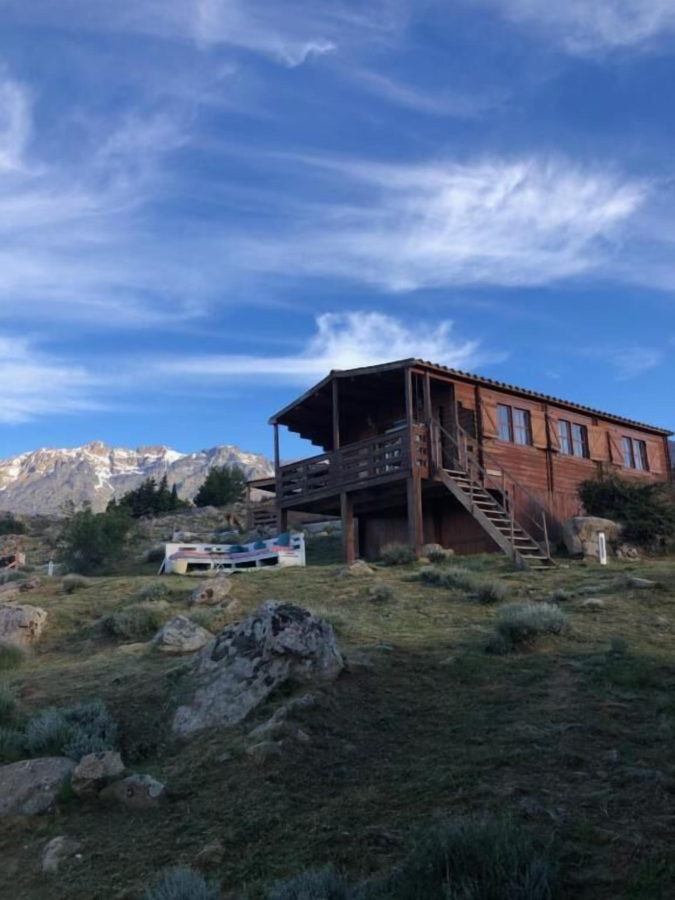 A wooden cabin with a balcony, set against a mountainous backdrop.