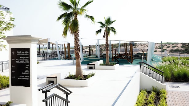 A modern outdoor area with palm trees, a play area, and a pool. - Bloomfields 2BR plus Maid in Yas Golf  (Abu Dhabi)