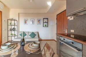 Eine moderne Küche mit Einbauofen, eine Essecke mit Tisch für Zwei und ein Wohnzimmer mit Sofa und Wandbildern.