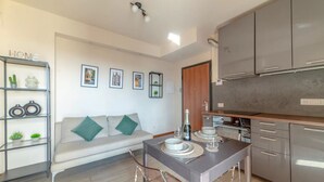 Een moderne keuken met grijze kastjes, een eettafel met stoelen, een bank met kussens en een wandplank met decoratieve objecten.