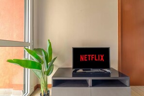Ein Fernseher auf einem Standfuß mit dem Netflix-Logo, einer Topfpflanze und einem Fenster.