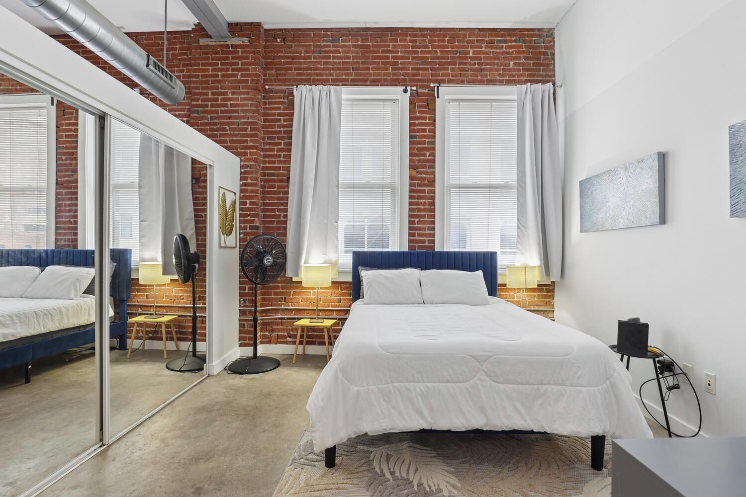 Une chambre avec un mur en briques, un lit avec une literie blanche, un bureau avec une chaise et un grand miroir.