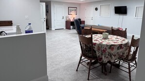 A spacious room with a dining table, chairs, and a kitchen area in the background.