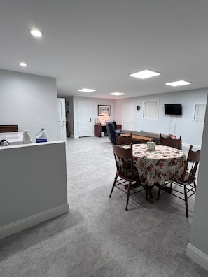 A spacious room with a dining table, chairs, and a kitchen area in the background.
