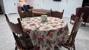 A dining area with a round table, floral tablecloth, and wooden chairs.